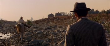 Movie still from “Chinatown” (1974), directed by Roman Polanski – A man wearing a suit and a hat is standing on a rocky hill; Extreme Wide shot, High angle
