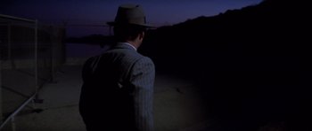 Movie still from “Chinatown” (1974), directed by Roman Polanski – A man wearing a suit and a hat is standing in the dark; Medium shot, Over the shoulder angle
