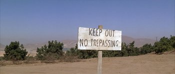 Movie still from “Chinatown” (1974), directed by Roman Polanski – A sign that reads " keep out no trespassing " on the side of the road; Extreme Wide shot, High angle