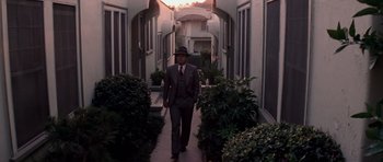 Movie still from “Chinatown” (1974), directed by Roman Polanski – A man in a suit and hat walking down a sidewalk; Wide shot, Low angle