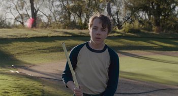 Movie still from “Wildlife” (2018), directed by Paul Dano – A young man holding a stick in a park; Medium shot, Over the shoulder angle
