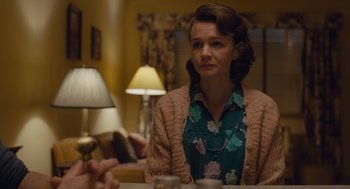 Movie still from “Wildlife” (2018), directed by Paul Dano – A woman sitting at a table in front of a lamp; Medium shot, Over the shoulder angle