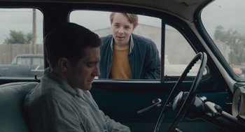 Movie still from “Wildlife” (2018), directed by Paul Dano – A young man looking out the window of a car while a young man sits in the driver's seat; Medium shot, Over the shoulder angle