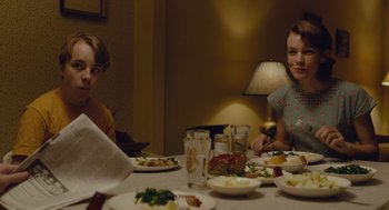 Movie still from “Wildlife” (2018), directed by Paul Dano – Two people sitting at a table with plates of food; Medium shot, Over the shoulder angle