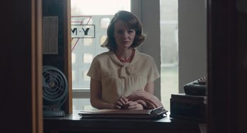 Movie still from “Wildlife” (2018), directed by Paul Dano – A woman sitting at a desk in front of an open book; Medium shot, Over the shoulder angle