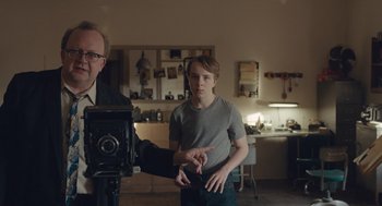 Movie still from “Wildlife” (2018), directed by Paul Dano – A young boy is being filmed by an older man; Medium shot, Over the shoulder angle