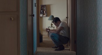 Movie still from “Wildlife” (2018), directed by Paul Dano – A man kneeling down in a living room; Wide shot, High angle