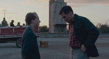 Movie still from “Wildlife” (2018), directed by Paul Dano – Two men standing next to each other on a dirt field; Medium shot, Over the shoulder angle