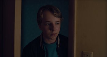 Movie still from “Wildlife” (2018), directed by Paul Dano – A young man looking at the camera in the dark; Close Up shot, Over the shoulder angle