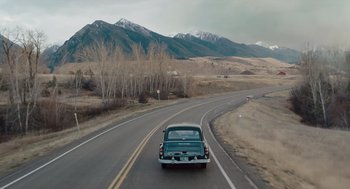 Movie still from “Wildlife” (2018), directed by Paul Dano – A car driving down a road near a mountain range; Extreme Wide shot, High angle