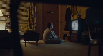 Movie still from “Wildlife” (2018), directed by Paul Dano – A person sitting on the floor watching television; Wide shot, High angle