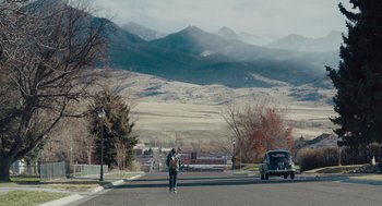 Movie still from “Wildlife” (2018), directed by Paul Dano – A person standing on the side of a road near a car; Extreme Wide shot, High angle