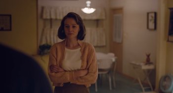 Movie still from “Wildlife” (2018), directed by Paul Dano – A woman standing with her arms crossed in a room; Medium shot, Over the shoulder angle