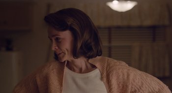 Movie still from “Wildlife” (2018), directed by Paul Dano – A woman in a pink sweater is smiling at the camera; Close Up shot, Over the shoulder angle