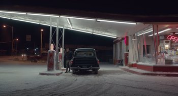Movie still from “Wildlife” (2018), directed by Paul Dano – A man standing next to an old car at a gas station; Wide shot, Over the shoulder angle