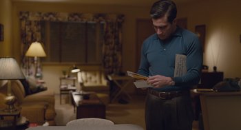Movie still from “Wildlife” (2018), directed by Paul Dano – A man standing in a living room holding an envelope; Medium shot, Low angle