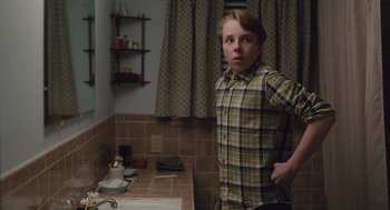 Movie still from “Wildlife” (2018), directed by Paul Dano – A young man standing in a bathroom next to a sink; Medium shot, Over the shoulder angle