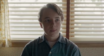 Movie still from “Wildlife” (2018), directed by Paul Dano – A young man in front of a window with blinds; Close Up shot, Over the shoulder angle