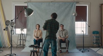 Movie still from “Wildlife” (2018), directed by Paul Dano – Two men and a woman sitting in front of a man taking a picture; Wide shot, Over the shoulder angle