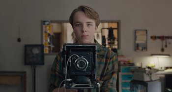 Movie still from “Wildlife” (2018), directed by Paul Dano – A young man holding an old camera in a living room; Close Up shot, Low angle