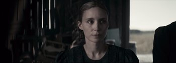 Movie still from “Women Talking” (2022), directed by Sarah Polley – A young woman with long blonde hair wearing a black dress; Close Up shot, Over the shoulder angle