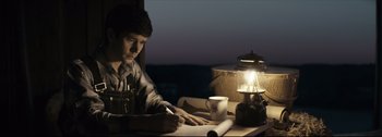 Movie still from “Women Talking” (2022), directed by Sarah Polley – A man sitting at a table writing on a piece of paper; Medium shot, High angle