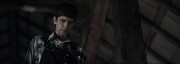Movie still from “Women Talking” (2022), directed by Sarah Polley – A young man holding a gun while standing next to a wooden structure; Close Up shot, Over the shoulder angle