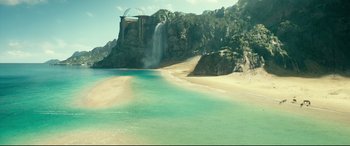 A beach with a waterfall and a bridge in the background