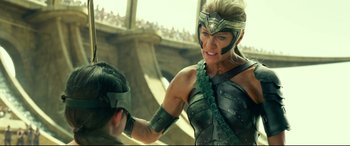 Movie still from “Wonder Woman 1984” (2020), directed by Patty Jenkins – A woman in a green and black costume holding a man in a black and green costume; Medium shot, Over the shoulder angle