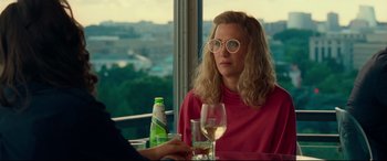 Movie still from “Wonder Woman 1984” (2020), directed by Patty Jenkins – A woman sitting at a table with a glass of wine; Medium shot, Over the shoulder angle