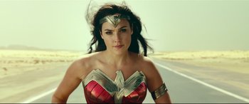 Movie still from “Wonder Woman 1984” (2020), directed by Patty Jenkins – A woman in a red and gold costume standing on the side of a road; Close Up shot, Low angle