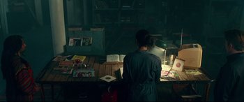 Movie still from “Wonder Woman 1984” (2020), directed by Patty Jenkins – A person standing in front of a table with books; Medium shot, High angle