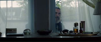 Movie still from “You Were Never Really Here” (2017), directed by Lynne Ramsay – A man sitting at a table looking out a window; Medium shot, Over the shoulder angle