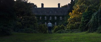 A man standing on a lush green field looking at a building