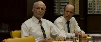 Movie still from “Zodiac” (2007), directed by David Fincher – Two older men sitting at a table in front of a window; Medium shot, Low angle