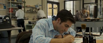Movie still from “Zodiac” (2007), directed by David Fincher – A man writing on a piece of paper in an office setting; Medium shot, Over the shoulder angle