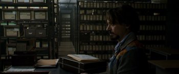 Movie still from “Zodiac” (2007), directed by David Fincher – A man sitting at a table in front of a book case; Medium shot, Over the shoulder angle