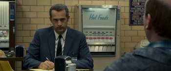 Movie still from “Zodiac” (2007), directed by David Fincher – A man in a suit and tie sitting at a table; Close Up shot, Over the shoulder angle