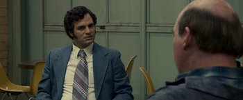 Movie still from “Zodiac” (2007), directed by David Fincher – A man in a suit and tie sitting at a table; Close Up shot, Over the shoulder angle