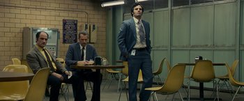 Movie still from “Zodiac” (2007), directed by David Fincher – A man in a suit and tie standing next to another man in a suit and tie; Medium shot, Low angle