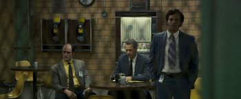 Movie still from “Zodiac” (2007), directed by David Fincher – A group of men sitting at a table in front of a brick wall; Medium shot, Low angle