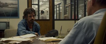 Movie still from “Zodiac” (2007), directed by David Fincher – A man sitting at a table in front of other people; Medium shot, Over the shoulder angle