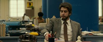 Movie still from “Zodiac” (2007), directed by David Fincher – A man sitting at a table with a pen and a cup; Medium shot, Low angle