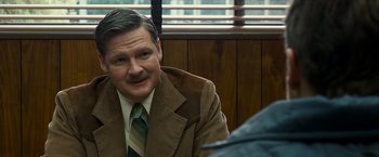 Movie still from “Zodiac” (2007), directed by David Fincher – An older man in a brown jacket and a striped neck tie; Close Up shot, Over the shoulder angle