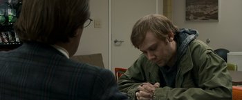 Movie still from “Zodiac” (2007), directed by David Fincher – A man sitting in front of another man writing on a piece of paper; Close Up shot, Over the shoulder angle