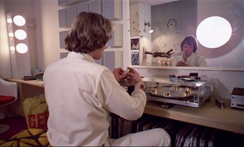 Movie still from “A Clockwork Orange” (1971), directed by Stanley Kubrick – A man sitting in front of a mirror holding something; Medium shot, High angle