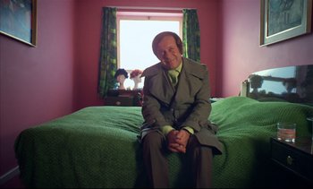 Movie still from “A Clockwork Orange” (1971), directed by Stanley Kubrick – A man sitting on top of a bed in a room; Medium shot, High angle