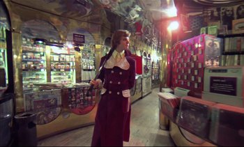 Movie still from “A Clockwork Orange” (1971), directed by Stanley Kubrick – A woman dressed in a long red coat holding a baseball bat in a store; Wide shot, Low angle