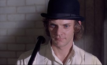 Movie still from “A Clockwork Orange” (1971), directed by Stanley Kubrick – A person wearing a hat and holding a cane; Close Up shot, Over the shoulder angle