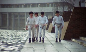 Movie still from “A Clockwork Orange” (1971), directed by Stanley Kubrick – A group of men walking down a sidewalk holding a baseball bat; Wide shot, High angle